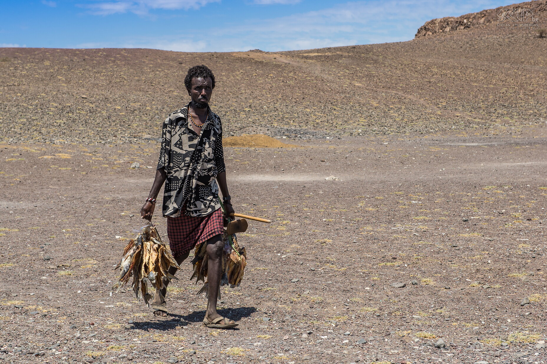 Lake Turkana - El Molo man Een man van de El Molo stam die met zijn visvangst naar huis komt. Hij draagt ook een traditionele houten hoofdsteun en stok. Stefan Cruysberghs